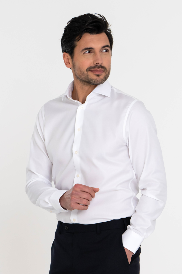 Jongeman opzij kijkend in een wit strijkvrij overhemd met lange mouwen en hand in zijn zak.