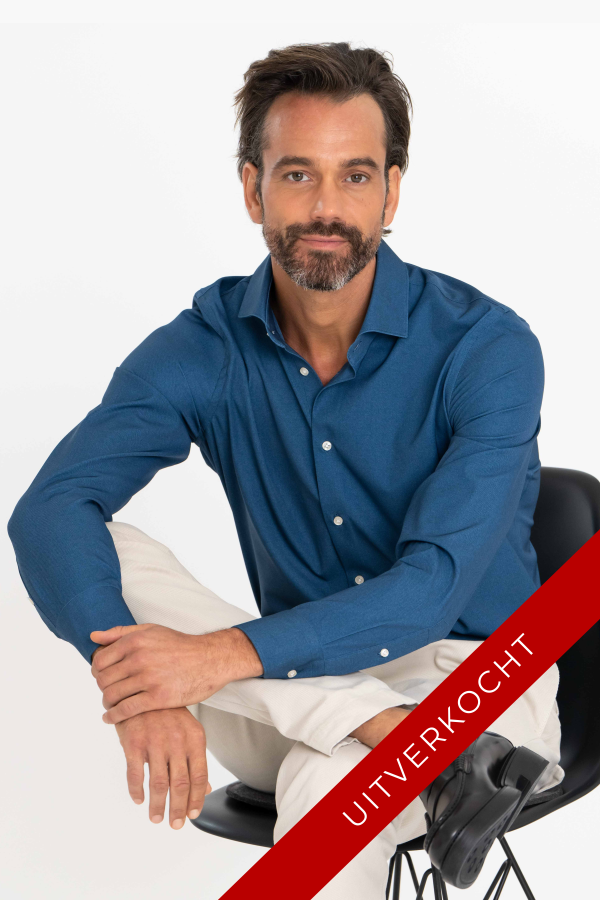 Gebruinde man met baardje zitten op een stoel in een donkerblauw techno twill shirt, met een been over de andere.